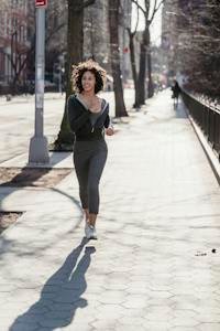 Full body of active young ethnic female millennial with dark curly hair in sportswear running on city street during morning workout on sunny day