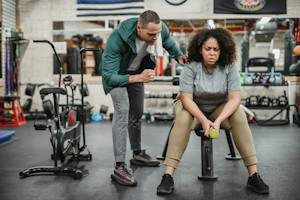 Personal male trainer with overweight female client in fitness center